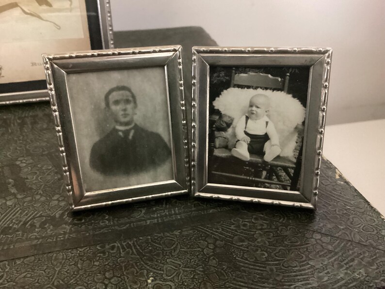May include: Two silver picture frames with black and white photos. The left frame shows a man in a suit and tie. The right frame shows a baby sitting in a chair.