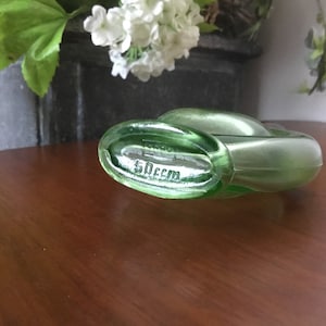 May include: A green glass bottle with a unique shape and a label that reads "50ccm".