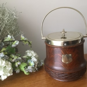 May include: A wooden cookie jar with a silver lid and handle. The jar has a decorative brass shield on the front.