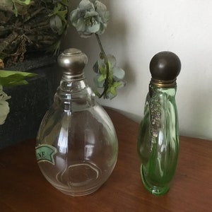 May include: Two vintage perfume bottles. One is clear glass with a silver top and a green label that says "ONE". The other is green glass with a brown top and a floral design.