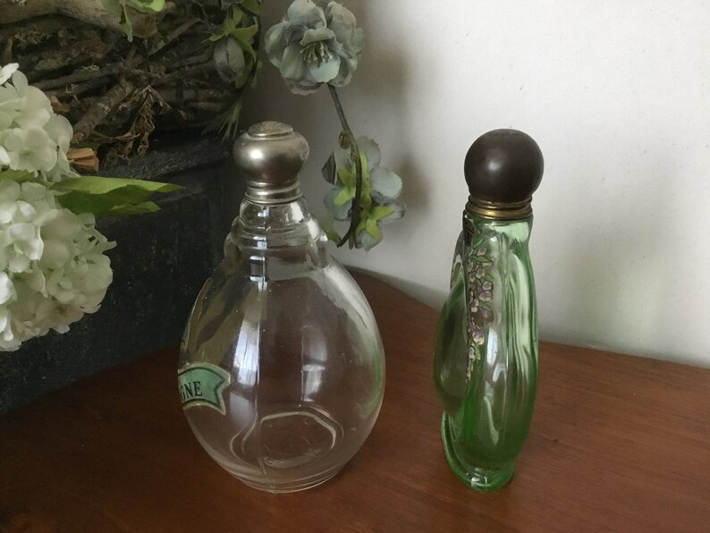 May include: Two vintage perfume bottles. One is clear glass with a silver top and a green label that says "ONE". The other is green glass with a brown top and a floral design.