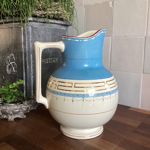 Puede incluir: Una jarra de cerámica azul y blanca con detalles dorados y un diseño decorativo. La jarra tiene una boca ancha y un asa.