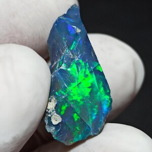 Puede incluir: Una piedra preciosa de ópalo en bruto, de color azul oscuro y verde, con destellos iridiscentes.