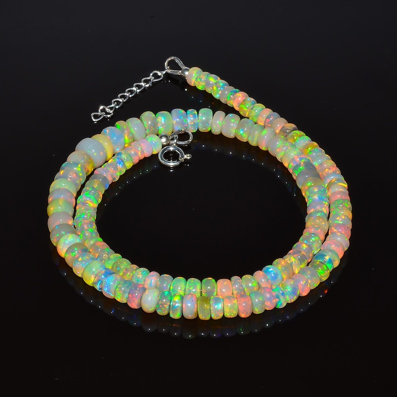 May include: A necklace made of iridescent opal beads. The beads are a mix of white, yellow, green, and pink, with flashes of blue and orange. The necklace has a silver clasp and chain extender.