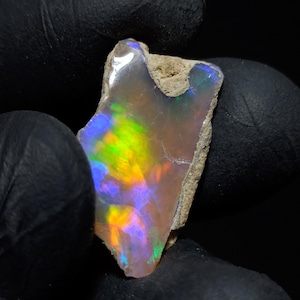 May include: A rough, iridescent opal with a rainbow of colors, including green, yellow, orange, and purple. The opal is set in a natural matrix.