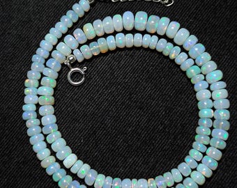 Könnte beinhalten: Eine Halskette mit mehreren Strängen aus ovalen Opalperlen. Die Perlen sind milchig weiß mit schillernden grünen und blauen Reflexen. Die Halskette wird mit einem silbernen Verschluss und einer Kette geschlossen.