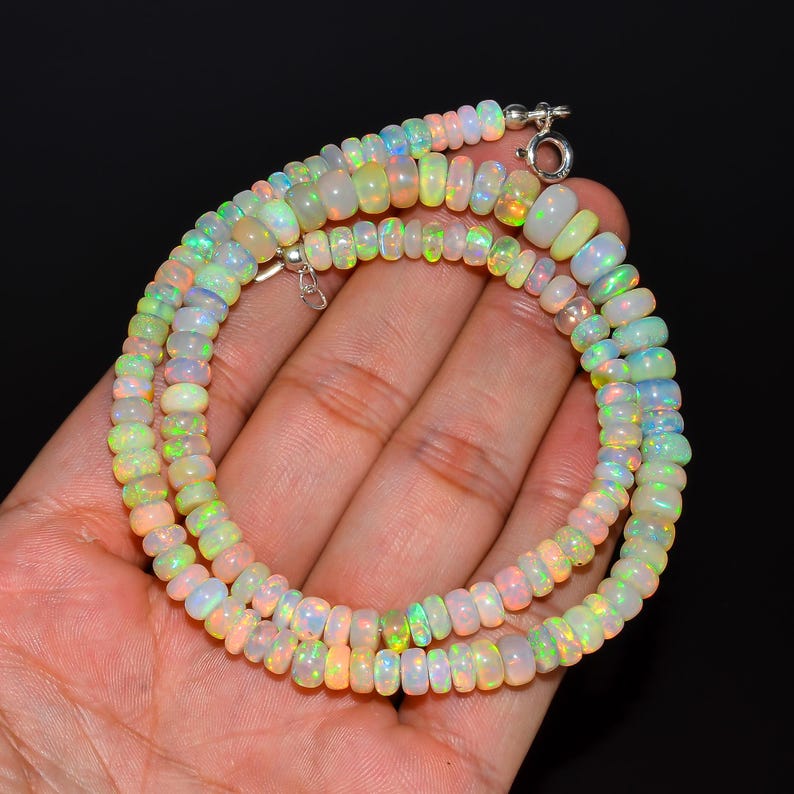 May include: A necklace featuring multiple strands of iridescent opal beads. The beads are a mix of white, yellow, and green, with flashes of colour. The necklace is secured with a silver clasp. The beads are approximately 0.6 cm in diameter.