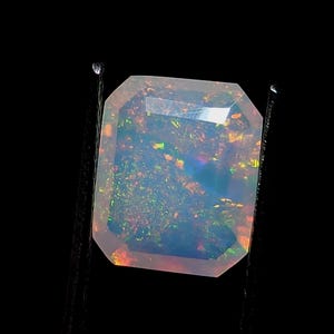 Könnte beinhalten: Ein hellblauer Opal-Edelstein mit rechteckiger Form und facettenreichem Schliff. Der Edelstein hat eine milchig weiße Basis mit grün, rot und orangefarbenen Blitzen.