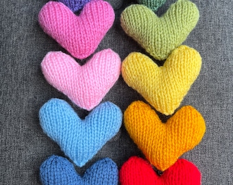 Könnte beinhalten: Ein Set aus zehn gestrickten Herzen in verschiedenen Farben, darunter Lila, Rosa, Grün, Gelb, Blau und Rot. Die Herzen sind in einem vertikalen Stapel angeordnet, wobei das größte Herz unten und das kleinste Herz oben liegt.