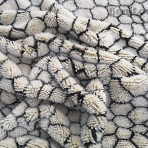 Könnte beinhalten: Nahaufnahme eines weißen und schwarzen gemusterten Stoffes mit einer flauschigen Textur. Der Stoff hat ein Wabenmuster.