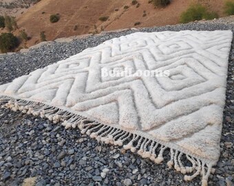 May include: White woven rug with a geometric pattern and fringe. The rug has a textured, fluffy surface.