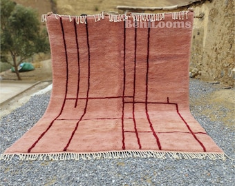 Puede incluir: Una alfombra geométrica de color rosa y rojo con flecos. La alfombra está hecha de lana y tiene un diseño tradicional marroquí.