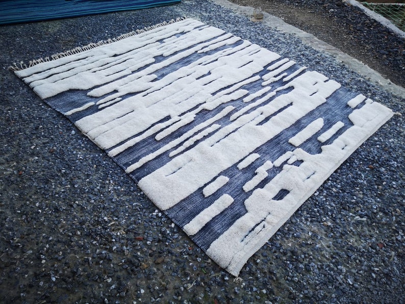 Op de afbeelding: Een modern abstract patroon tapijt met een franje rand. Het tapijt heeft een modern ontwerp met verticale strepen en onregelmatige vormen.