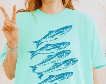 May include: A light blue t-shirt with a graphic of five blue fish swimming in a row.