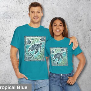 K&ouml;nnte beinhalten: Zwei Personen tragen t&uuml;rkisfarbene T-Shirts mit einem grafischen Design einer Meeresschildkr&ouml;te und Fischen in einem quadratischen Rahmen. Der Text "Tropical Blue" befindet sich am unteren Rand des Bildes.