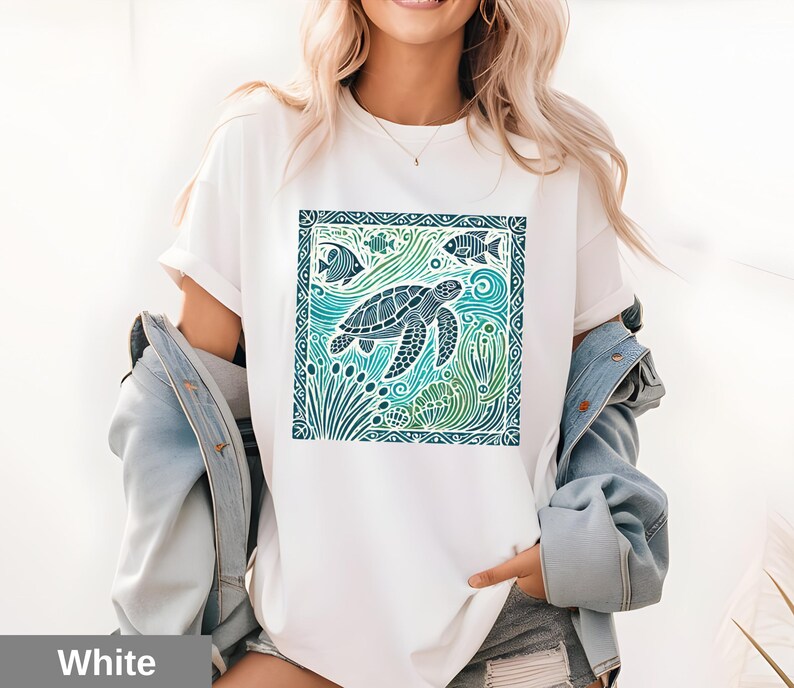 K&ouml;nnte beinhalten: Wei&szlig;es T-Shirt mit einem grafischen Aufdruck einer Meeresschildkr&ouml;te, die in einer blauen und gr&uuml;nen Ozeanszene schwimmt. Das Design ist in einem dunkelblauen Rahmen eingefasst.