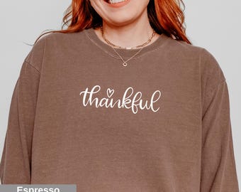 May include: Espresso-colored sweatshirt with the word "thankful" in white script, featuring a small heart. The sweatshirt has a crew neck and long sleeves. The color is a warm, earthy brown.