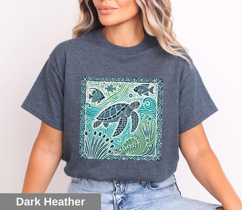 K&ouml;nnte beinhalten: Ein dunkel-helles graues T-Shirt mit einem grafischen Aufdruck einer Meeresschildkr&ouml;te, die in einer blauen und gr&uuml;nen Ozeanszene schwimmt. Das Design ist von einem dekorativen Rahmen umgeben.