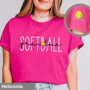 Puede incluir: Camiseta rosa con el texto "Softball grandma" en blanco con un gráfico de softball amarillo.