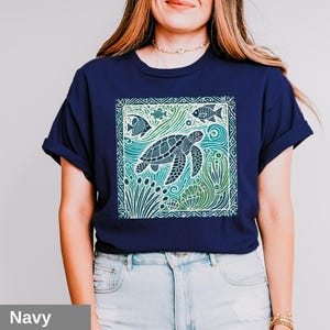 K&ouml;nnte beinhalten: Ein marineblaues T-Shirt mit einem grafischen Aufdruck einer Meeresschildkr&ouml;te, die in einem Korallenriff schwimmt. Das Design ist in einer Farbpalette aus Gr&uuml;n, Blau und Wei&szlig; gehalten.