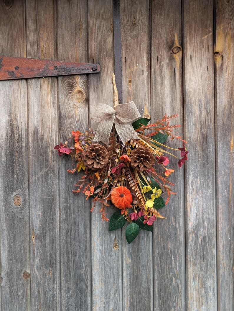 Pu&ograve; includere: Una decorazione autunnale composta da due pigne marroni, una piccola zucca arancione e un assortimento di fogliame artificiale nei toni del rosso, arancione, giallo e verde. Un fiocco in juta beige &egrave; legato sulla parte superiore dell'insieme.