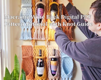 Könnte beinhalten: Macrame-Weinständer mit vier Flaschenhaltern. Der Ständer ist aus naturfarbenem Kordel gefertigt und hat ein hellblaues, braunes und senfgelbes Farbschema. Der Ständer hängt an einer Wand mit vier Flaschen Wein in den Haltern.