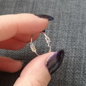 Può includere: Un anello d'argento con un design delicato. L'anello è aperto e ha un piccolo cerchio al centro.