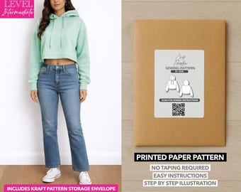 May include: A woman wearing a mint green cropped hoodie and blue jeans. Next to her is a brown paper pattern envelope with a white label that reads "Crop Hoodie Sewing Pattern" and includes a QR code and the text "Printed Paper Pattern".