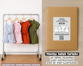 May include: A clothing rack displays four girls' rompers in various colors and styles: blue striped, pink polka dot, rust-colored, and olive green. A kraft paper envelope with a sewing pattern label is also visible, with the text "GIRLS ROMPER SEWING PATTERN BUNDLE".