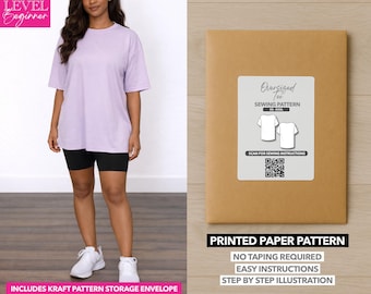 Op de afbeelding: Een vrouw draagt een oversized lavendelkleurig T-shirt en een zwarte fietsbroek, gecombineerd met witte sneakers. Een bruine papieren patroon-envelop met een wit label met de tekst "Oversized Tee Sewing Pattern" is ook zichtbaar. De tekst "Printed Paper Pattern" staat onderaan.