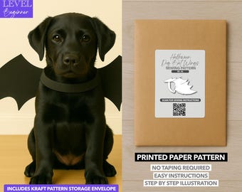 May include: A black Labrador puppy wearing a black bat wing costume. The image includes a brown paper pattern envelope with a label that reads "Halloween Dog Bat Wings Sewing Pattern". The pattern is a beginner level.