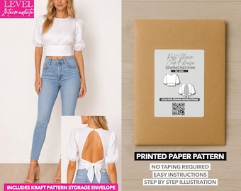 May include: A woman wearing a white puff sleeve crop blouse and light blue jeans. A brown paper envelope with a label that reads "Puff Sleeve Crop Blouse Sewing Pattern" is also shown. The text "Printed Paper Pattern" is visible.