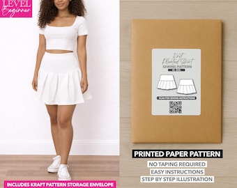Op de afbeelding: Een vrouw draagt een witte crop top en een geplooide rok. Naast haar staat een bruine papieren patroon envelop met het label "Knit Pleated Skirt Sewing Pattern". De tekst "Printed Paper Pattern" is ook zichtbaar.