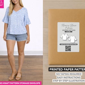 May include: A woman wearing a blue floral blouse and denim shorts. Next to her is a brown paper pattern envelope with a label that reads "Flounce Sleeve Blouse Sewing Pattern." The envelope also states "Printed Paper Pattern" and "No Taping Required."