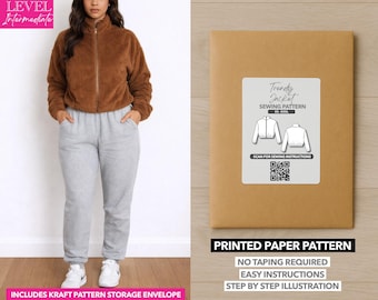 Op de afbeelding: Een vrouw draagt een bruine jas met ritssluiting en een grijze joggingbroek. Naast haar staat een bruine papieren patroon envelop met een wit label met de tekst "Trendy Jacket Sewing Pattern". Het patroon bevat een QR-code.