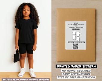 Op de afbeelding: Een jong persoon draagt een zwart T-shirt, zwarte biker shorts en witte sneakers, met een zwarte draagtas. Daarnaast een bruine papieren patroon envelop met het label "GIRLS TEE + BIKER SHORTS SET SEWING PATTERN".