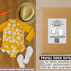 May include: A yellow girls' swimsuit with white daisy patterns, long sleeves, and a front zipper. The image also shows a sewing pattern envelope with the text "GIRLS ZIPPER FRONT SWIMSUIT SEWING PATTERN". Other items include orange sunglasses, a straw hat, and white flip-flops.