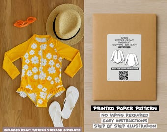 Op de afbeelding: Een gele meisjesbadpak met witte madeliefpatronen, lange mouwen en een ritssluiting aan de voorkant. De afbeelding toont ook een naaipatroon-envelop met de tekst "GIRLS ZIPPER FRONT SWIMSUIT SEWING PATTERN".
