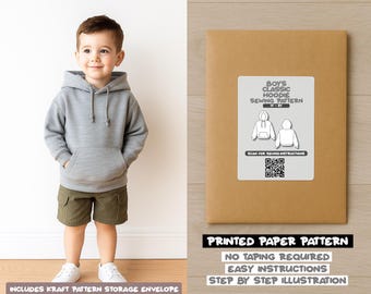 May include: A young child wearing a gray hoodie and olive green shorts. Beside the child is a brown paper pattern envelope with a label that reads "BOYS CLASSIC HOODIE SEWING PATTERN". The envelope also states "PRINTED PAPER PATTERN".