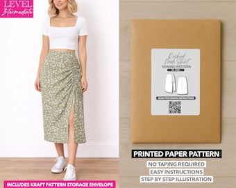 May include: A woman wearing a white crop top and a green floral print skirt with a side slit. Next to her is a brown paper pattern envelope with a label that reads "Ruched Mick Skirt Sewing Pattern". The text "Printed Paper Pattern" is also visible.