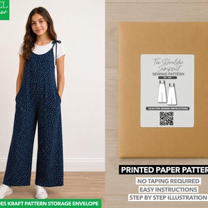 Peut inclure: Une combinaison bleu marine à motif moucheté blanc, avec des bretelles à nouer et des jambes larges, portée sur un t-shirt blanc. À côté se trouve une enveloppe en papier kraft contenant un patron de couture imprimé pour cette combinaison.