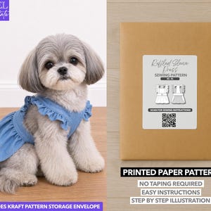Op de afbeelding: Een kleine, pluizige hond met een blauwe spijkerjurk met ruches zit naast een bruine papieren patroon-envelop. De envelop heeft een label met de tekst "Ruffled Sleeve Dress Sewing Pattern" en bevat een QR-code.