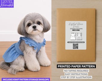May include: A small, fluffy dog wearing a blue denim dress with ruffled sleeves sits next to a brown paper pattern envelope. The envelope has a label that reads "Ruffled Sleeve Dress Sewing Pattern" and includes a QR code.