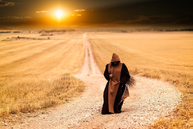 May include: A person wearing a brown hooded robe walks down a dirt road in a field of dry grass. The sun is setting in the background.