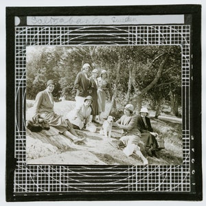 May include: A black and white photograph of a group of women in hats and dresses, standing and sitting in a wooded area. A small dog is in the centre of the photo. The text "Saltzbauren Sweden" is written at the top of the photo.