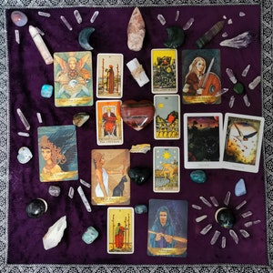 May include: A tarot card reading spread on a purple velvet surface with crystals and stones. The cards include The Empress, The Emperor, The Star, The High Priestess, Shield Maiden, King of Pentacles, The Lovers, The Sun, and Strength.