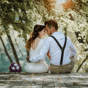 May include: A couple in wedding attire, sitting on a wooden deck, with a bouquet of purple and white flowers in front of them. They are looking at each other and smiling.