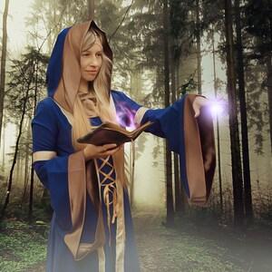 May include: A woman wearing a blue and brown hooded robe casts a spell with a book in a misty forest setting.