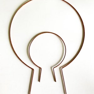 May include: Two copper wire headbands, one larger than the other, are shown on a white background. The headbands are both circular in shape and have a slight bend at the bottom.