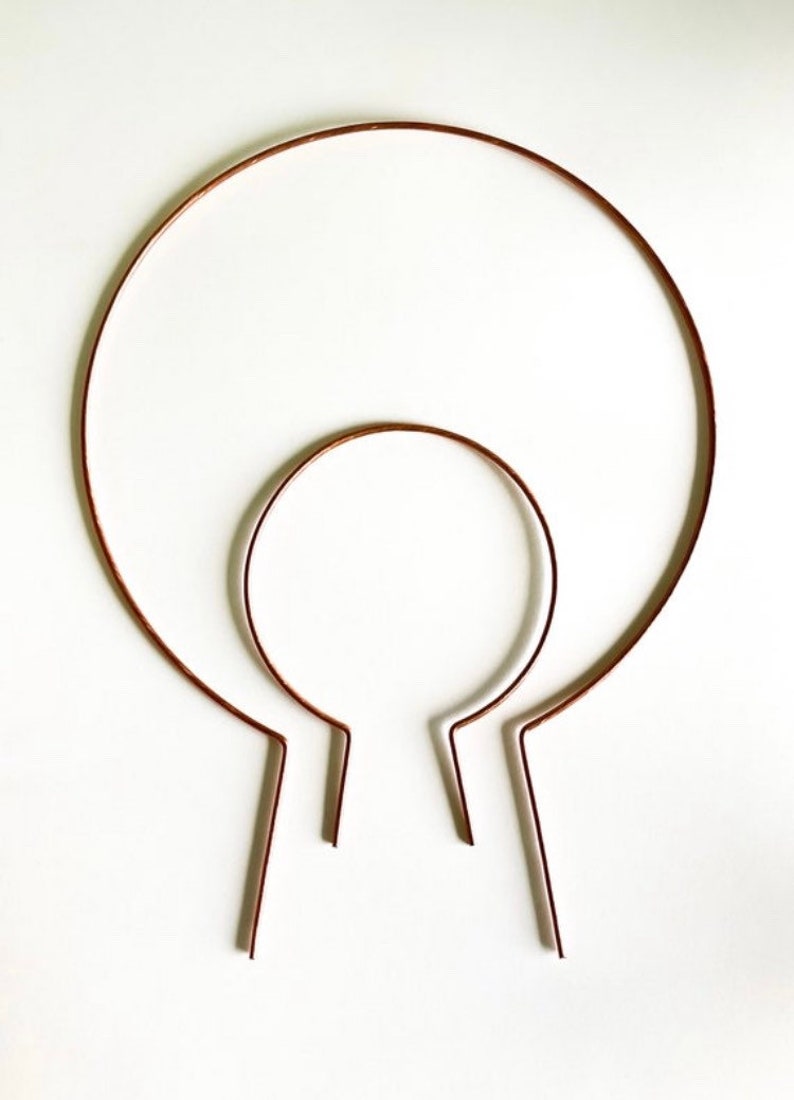May include: Two copper wire headbands, one larger than the other, are shown on a white background. The headbands are both circular in shape and have a slight bend at the bottom.